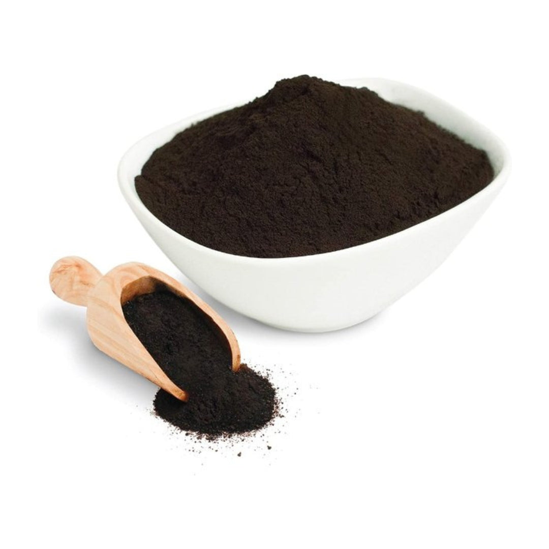 White ceramic bowl filled with dark brown Shilajit powder, accompanied by a wooden scoop.