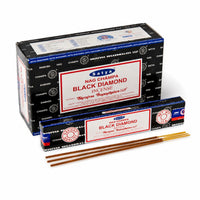 Satya Black Diamond incense stick burning in a wooden holder with smoke rising, grounding ritual setup