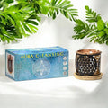 Aura Cleansing incense box with a decorative candle holder on a white background with green leaves.