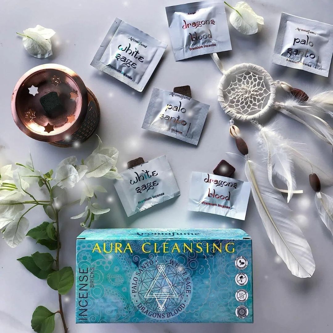 Aura Cleansing incense packaging with various incense packets, a dreamcatcher, and flowers on a light background.