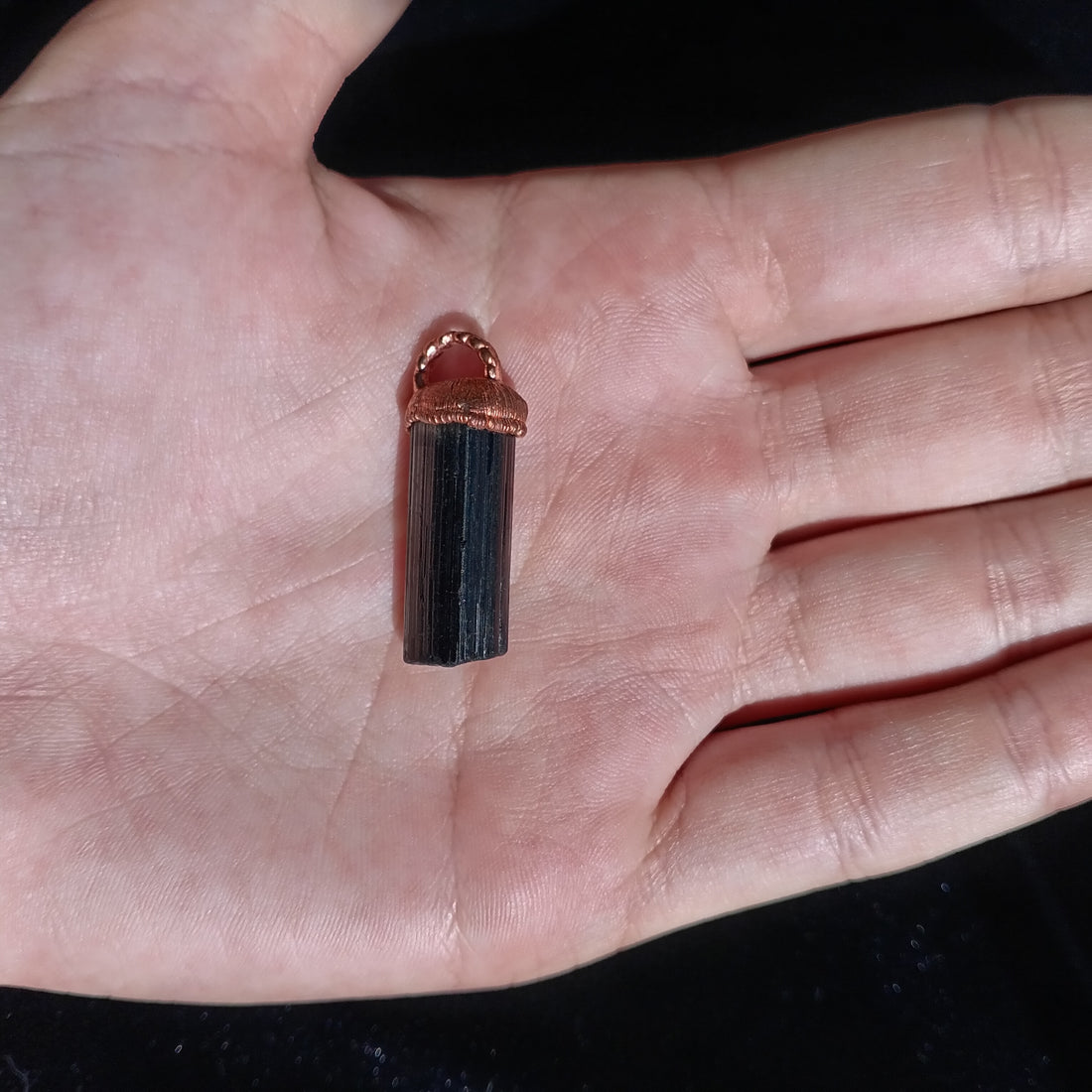 Black Tourmaline crystal pendant with copper cap resting on an open palm — grounding energy jewellery by Secret Sense