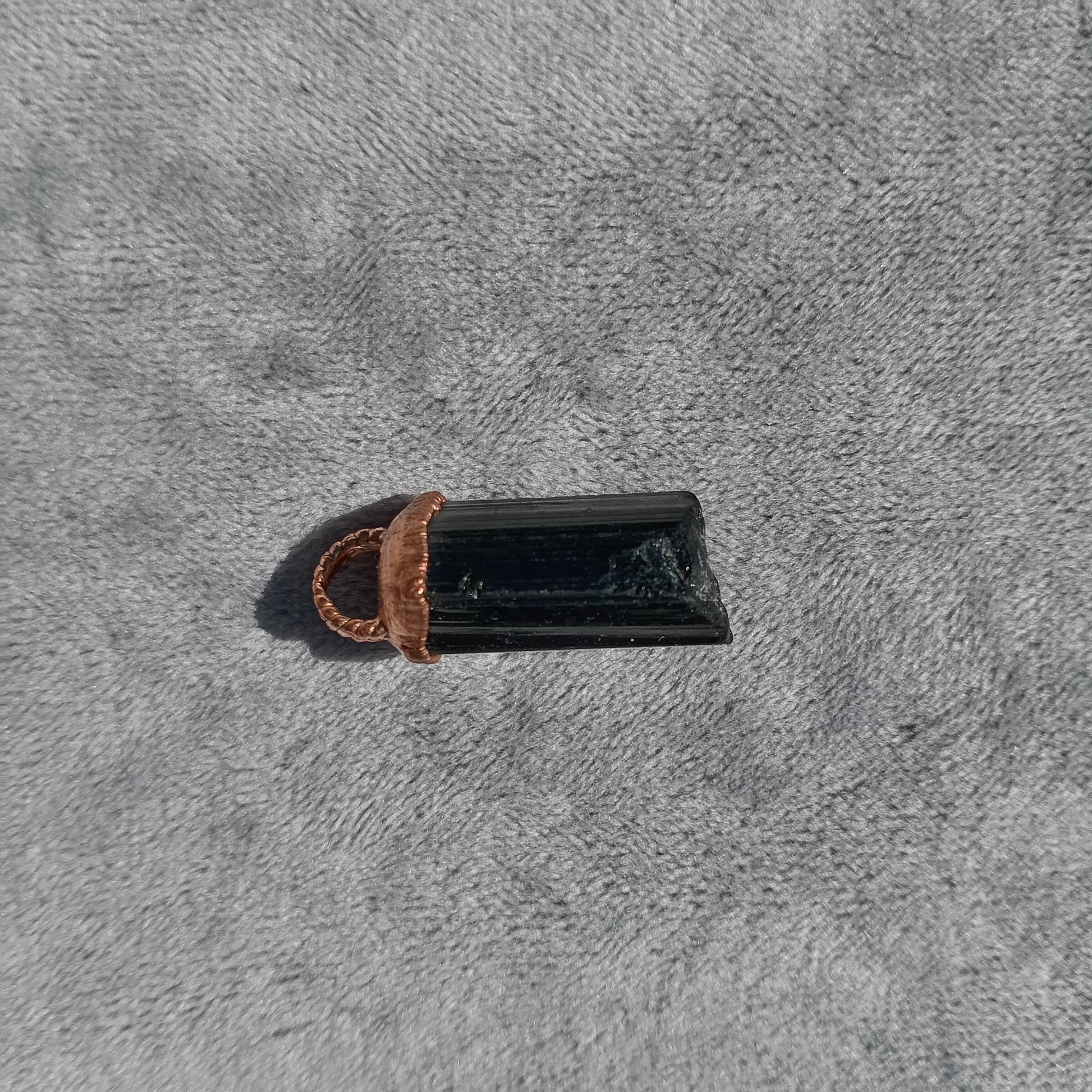 Front view of polished Black Tourmaline pendant capped in copper, photographed upright
