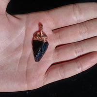 Obsidian arrowhead crystal in the palm of a hand, showcasing its sleek, dark surface.
