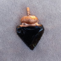 Single obsidian arrowhead pendant laying flat, highlighting its sharp, precise shape.