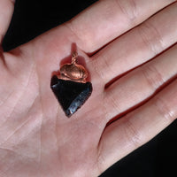 Close-up of an obsidian arrowhead pendant in the palm of a hand, highlighting its sharp edges.