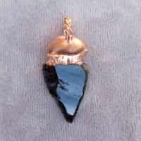 Obsidian arrowhead crystal pendant close-up, showcasing its smooth and glossy texture.