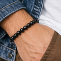 Black Obsidian Crystal bracelet on a wrist with denim and brown pants.