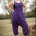 Person wearing purple overalls standing in a field with trees in the background