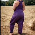 Person wearing purple overalls standing in a field with hay bales.