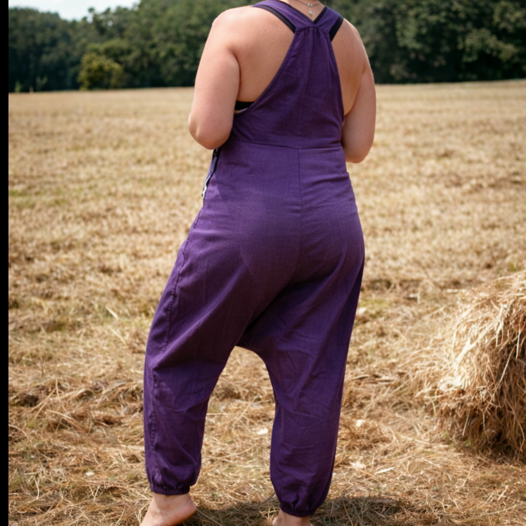 Person wearing purple overalls standing in a field with hay bales.
