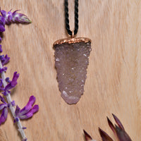 Spirit quartz pendant on black cord with copper top displayed next to purple lavender