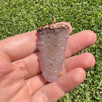 Spirit quartz pendant with copper electroplating held in hand on grass background