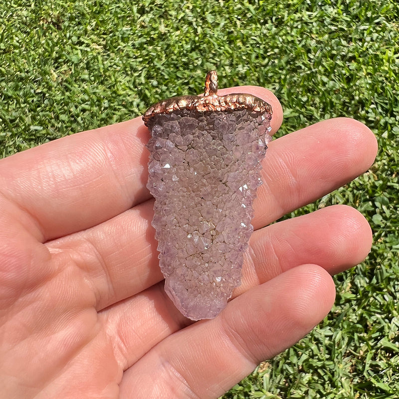 Spirit quartz pendant with copper electroplating held in hand on grass background